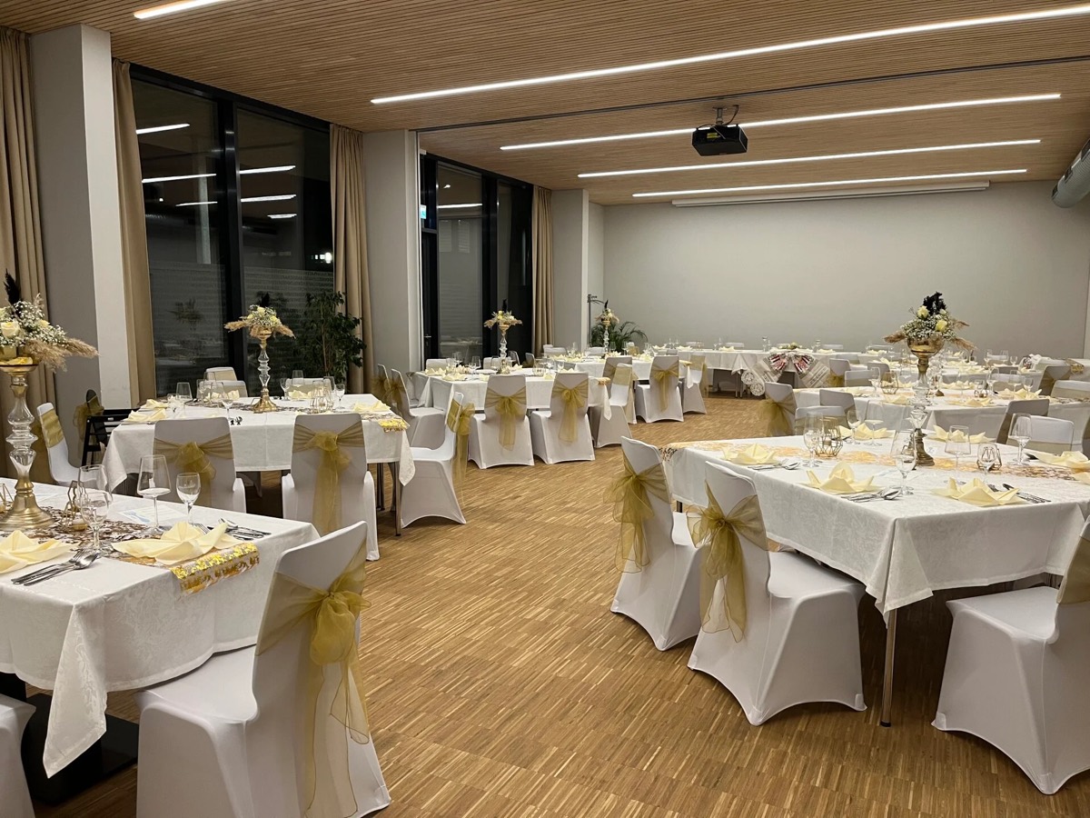 Eine Hochzeitsfeier im Q5: eine lange festliche Tafel mit weißen Läufern, Kerzen und Blumen, warmes Abendlicht im Raum.
